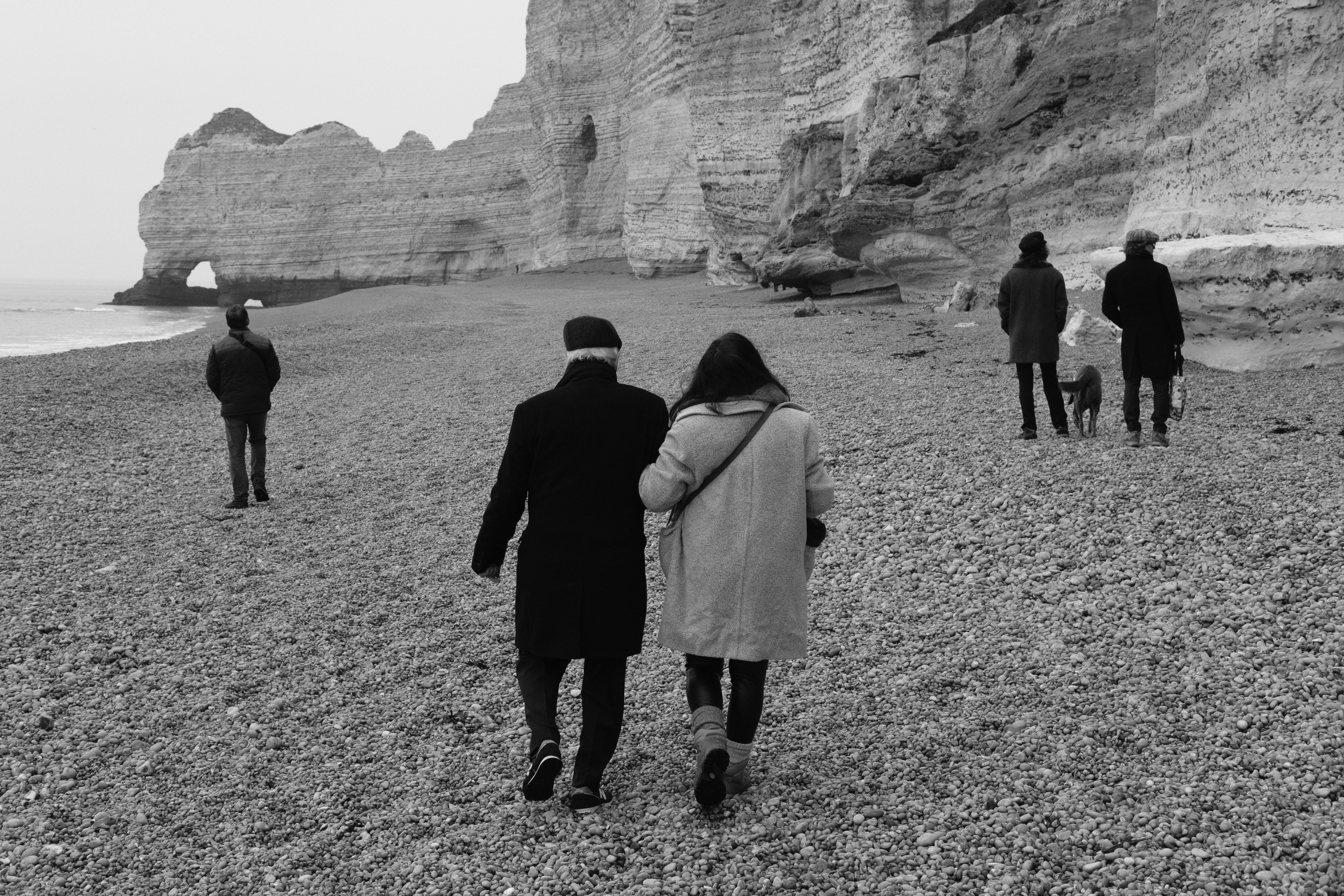 People walking along the pebble beach near the famous cliffs of Etretat, France in a black and white setting.
