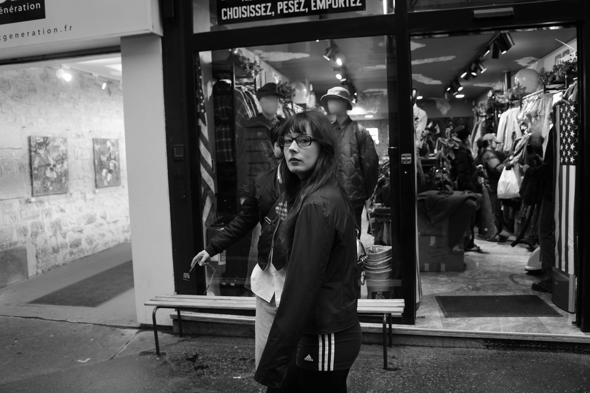 Black and white photo of a woman outside a vintage clothing store doorway.