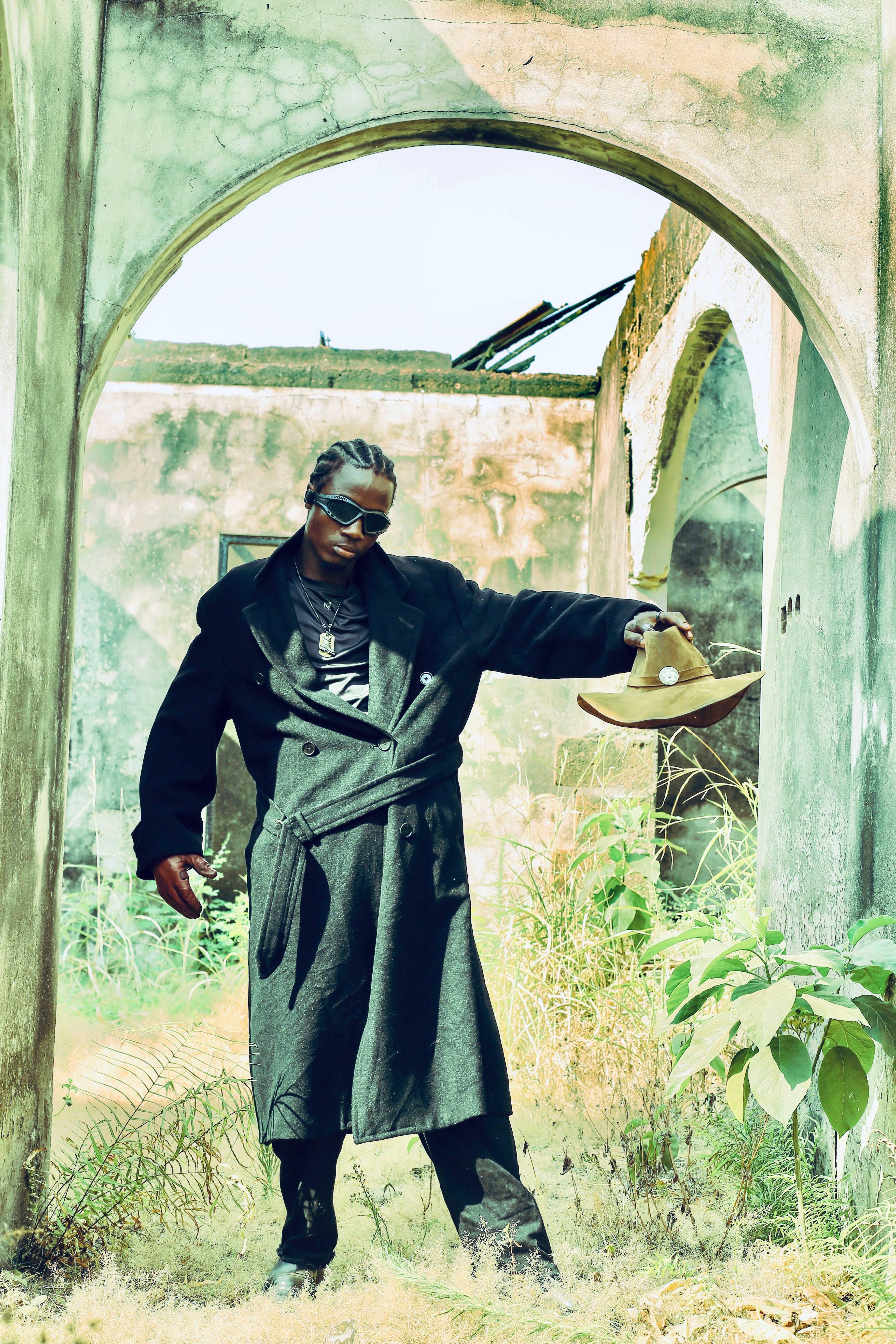 Fashionable man in sunglasses posing confidently in a rustic archway, exuding modern style.