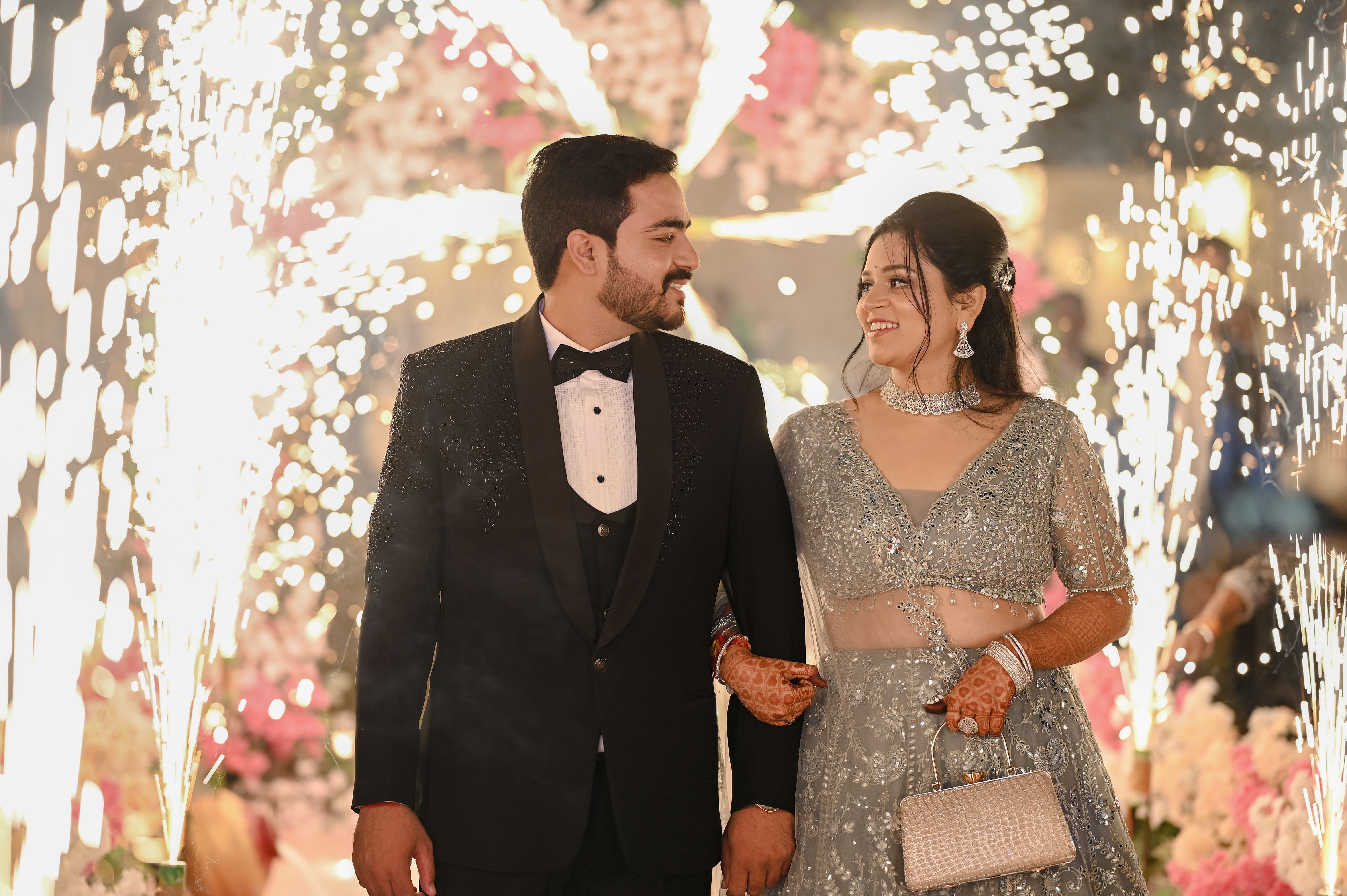 A couple dressed in formal attire celebrating at a glamorous wedding with fireworks.