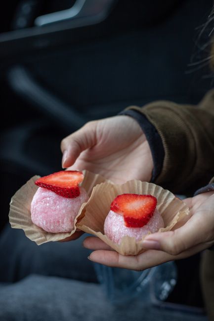 Close-up of hands holding pink strawberry mochi with fresh slices, showcasing a sweet treat.