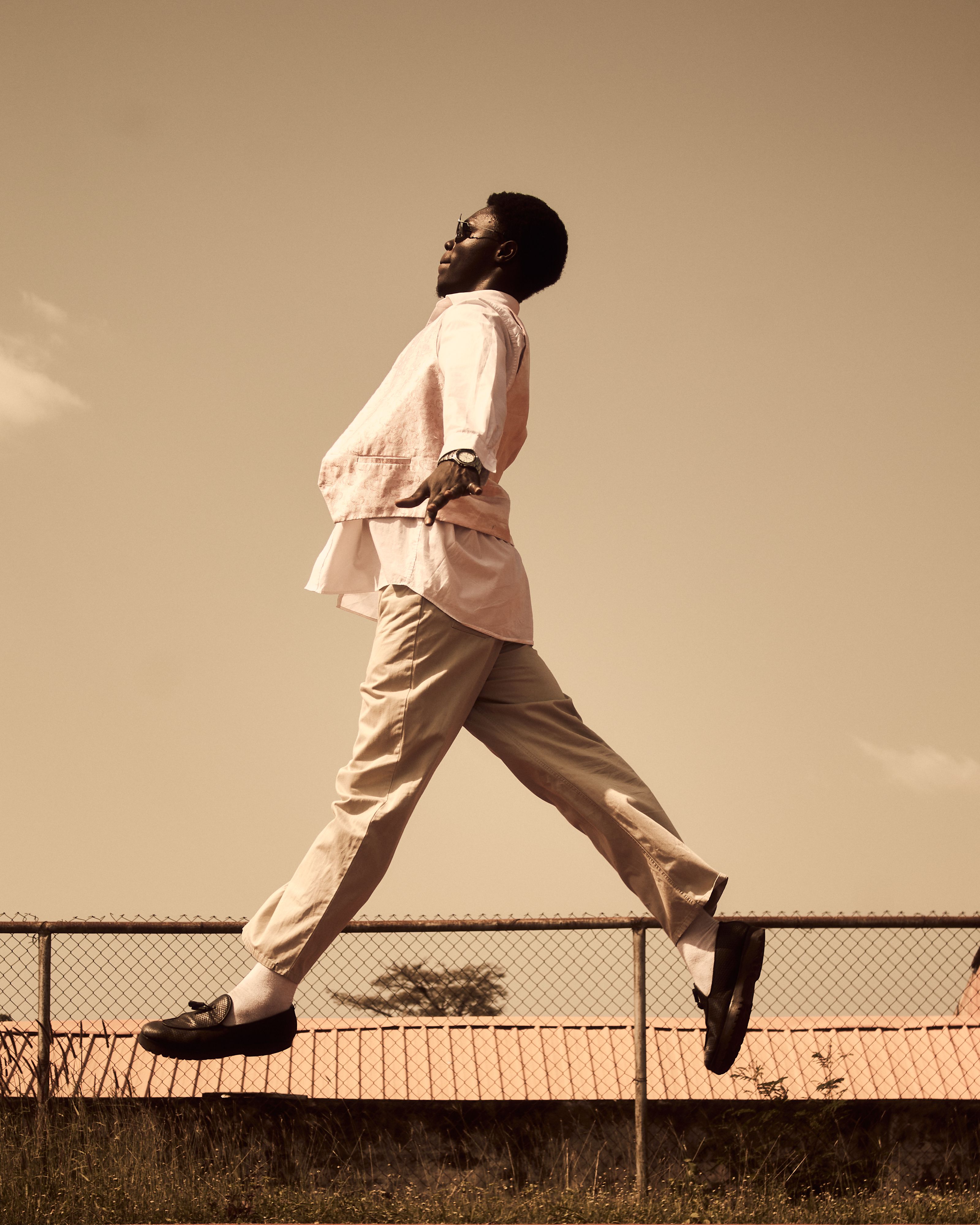A joyful adult man leaps mid-air outside over a fence, captured in sepia tones.