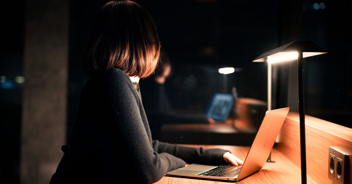 A woman works on her laptop under warm lighting, creating a calm nighttime atmosphere.