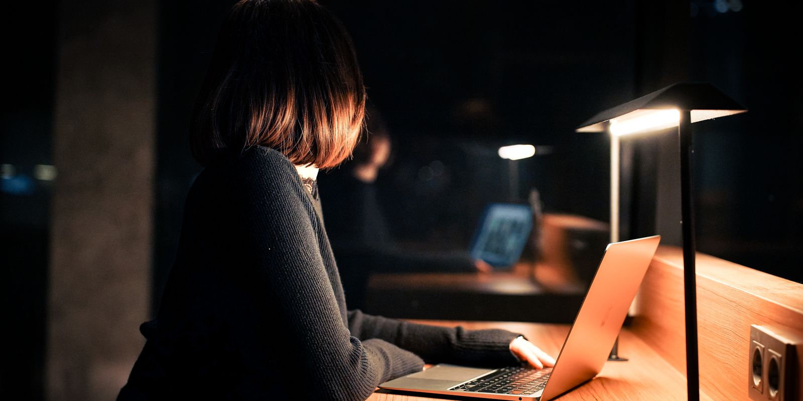 A woman works on her laptop under warm lighting, creating a calm nighttime atmosphere.