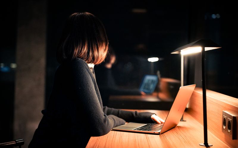 A woman works on her laptop under warm lighting, creating a calm nighttime atmosphere.