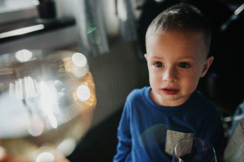 Free A young child intrigued by light reflections on a glass, indoors with a warm atmosphere. Stock Photo