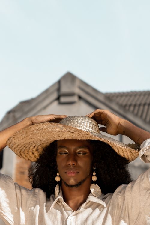 Free Elegant portrait of a woman with a straw hat and earrings, set against a rustic background. Stock Photo