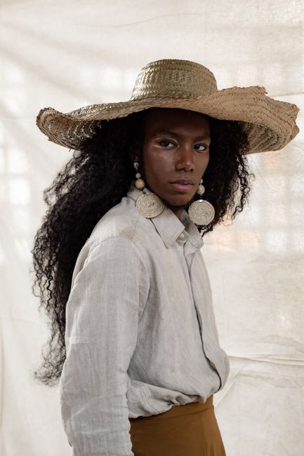 Stylish portrait of a fashionable person wearing a straw hat and expressive earrings in a serene setting.