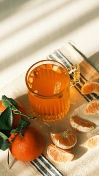 A refreshing glass of tangerine juice with fresh fruit and leaves on a striped cloth.