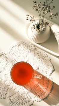 Aesthetic afternoon tea in glass cup on lace doily with soft sunlight.