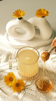 Warm still life of tea with honey and flowers on a textured surface.