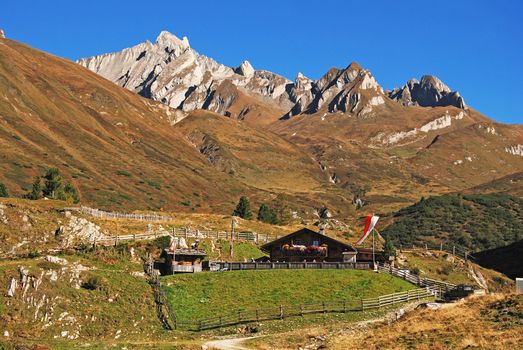 Charming wooden cabin nestled in the Alps, surrounded by lush green hills and rugged peaks.