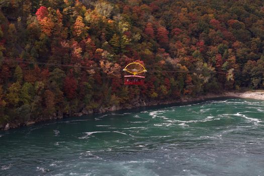 A stunning autumn view of the Niagara Whirlpool Aero Car over the river and vibrant fall foliage.