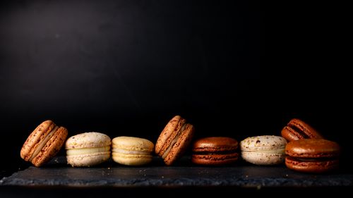 Free A row of colorful macarons arranged on slate against a dark background, highlighting their elegance and variety. Stock Photo