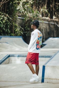 Stylish young man wearing colorful streetwear stands in an urban skate park.