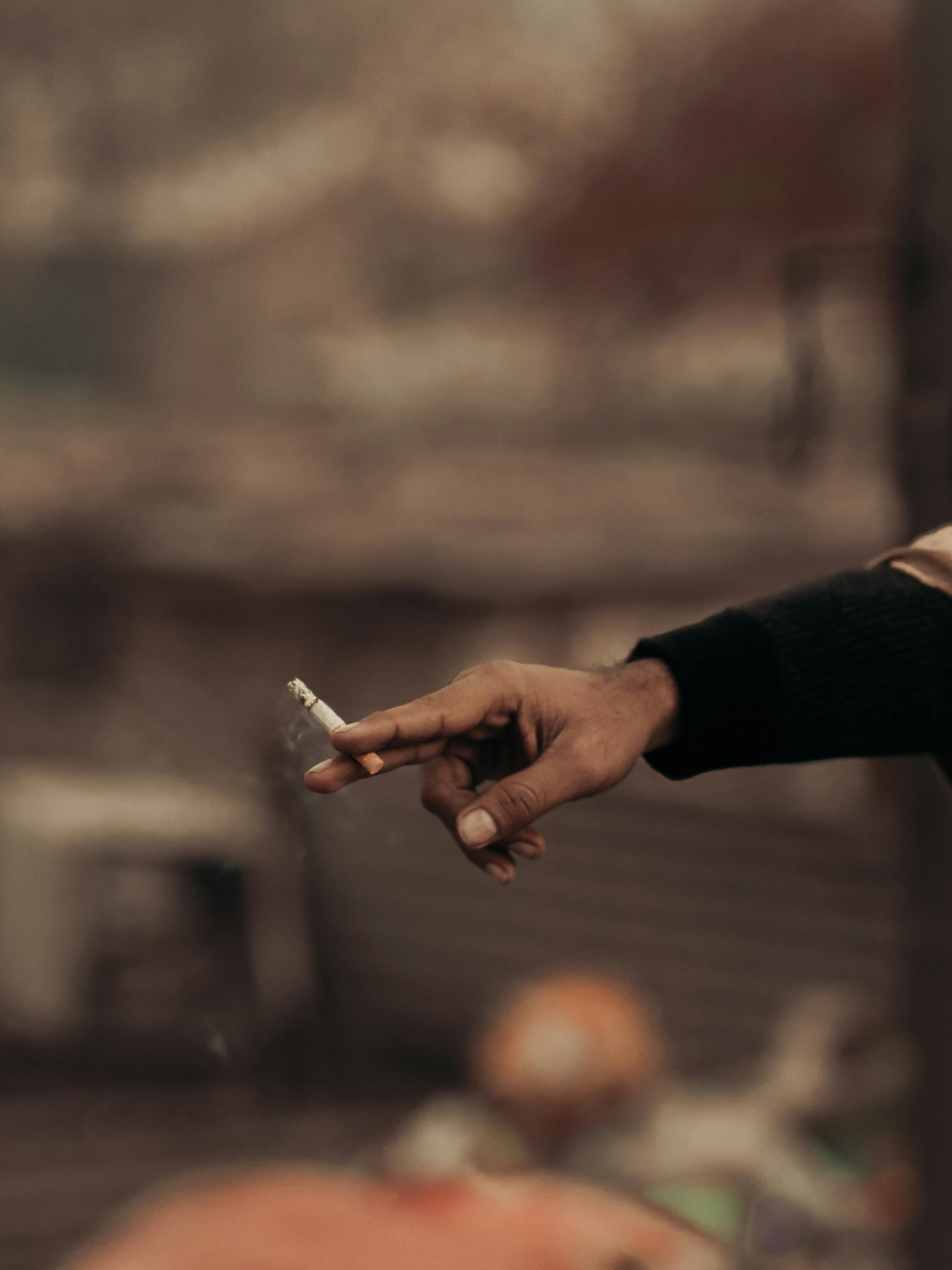 Gratis Un primer plano de una mano adulta sosteniendo un cigarrillo con un fondo borroso. Foto de stock