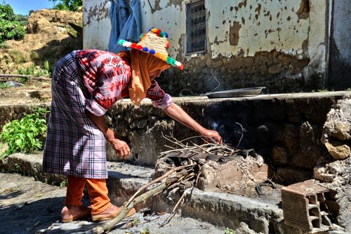Free Woman in colorful attire tends to outdoor traditional stove in Taounate, Morocco. Stock Photo