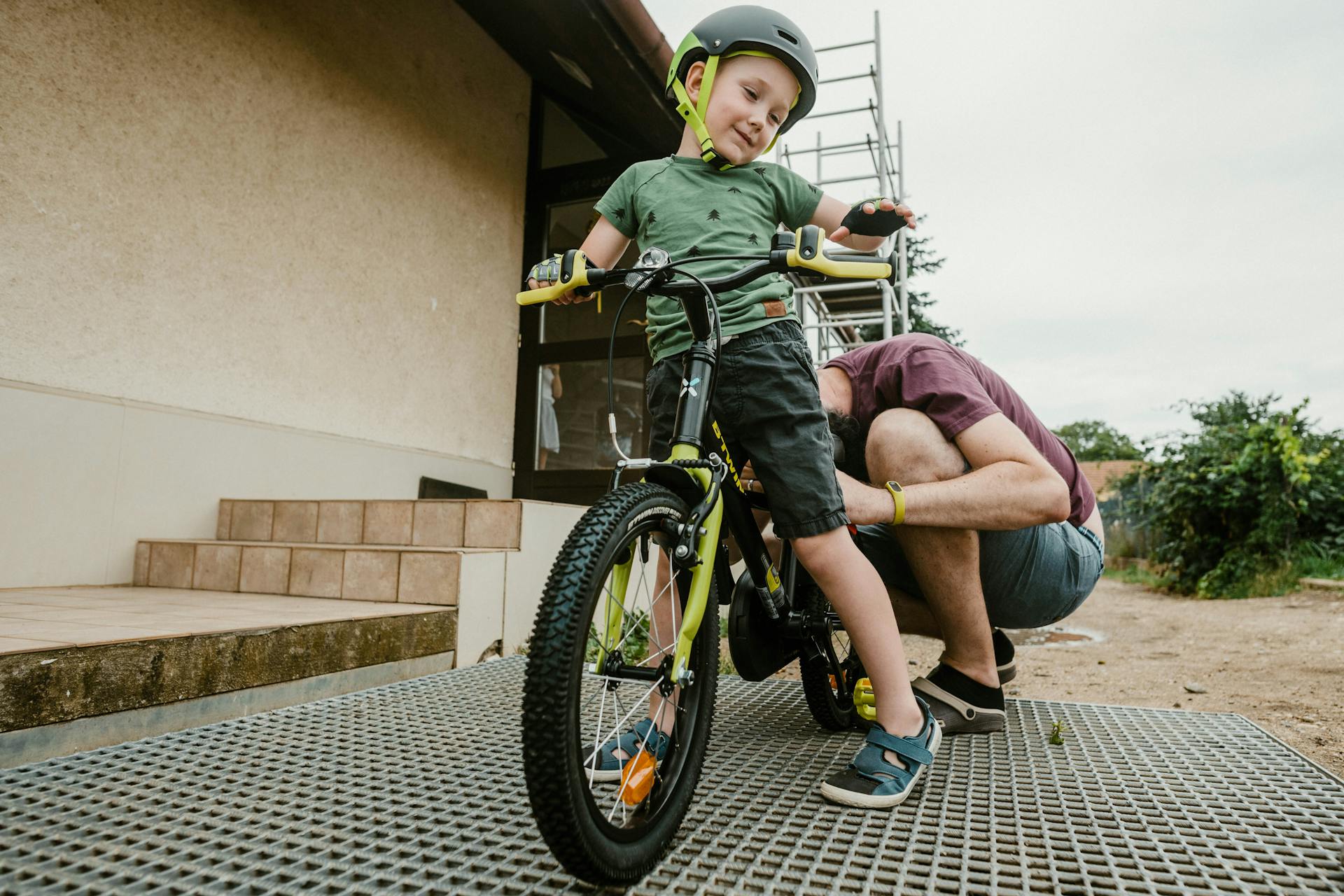 Father assisting young son with bicycle in backyard, teaching safe riding.