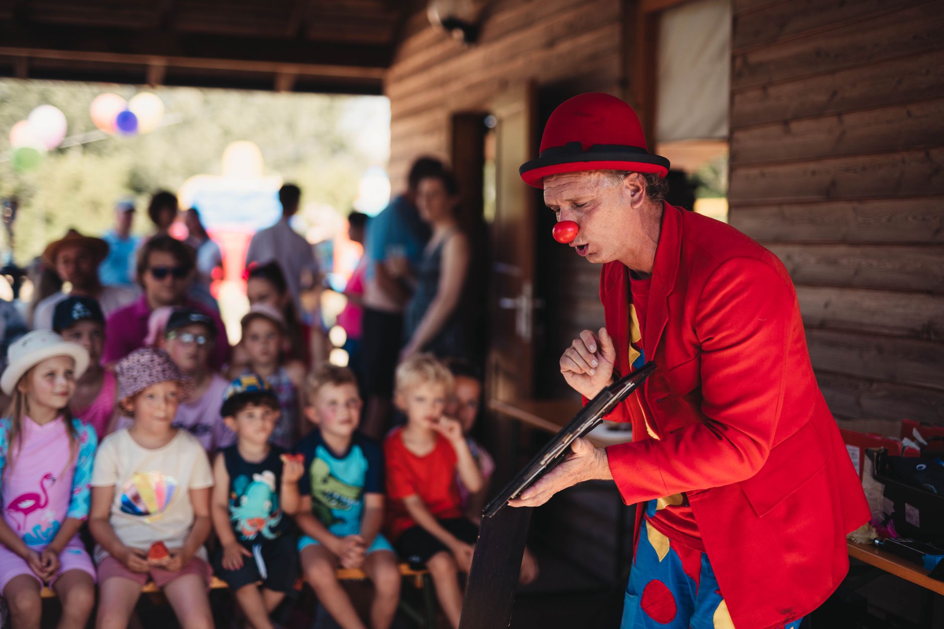 juggler for kids party cairo — A lively clown performing for a group of children during a sunny outdoor event.