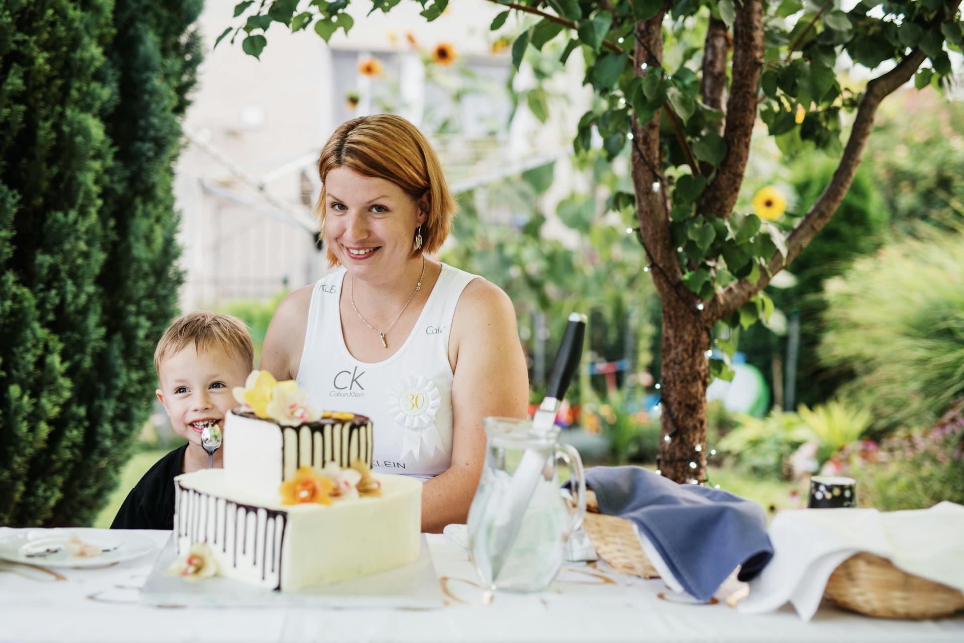 A joyful mother and child celebrating a birthday outdoors with a cake.