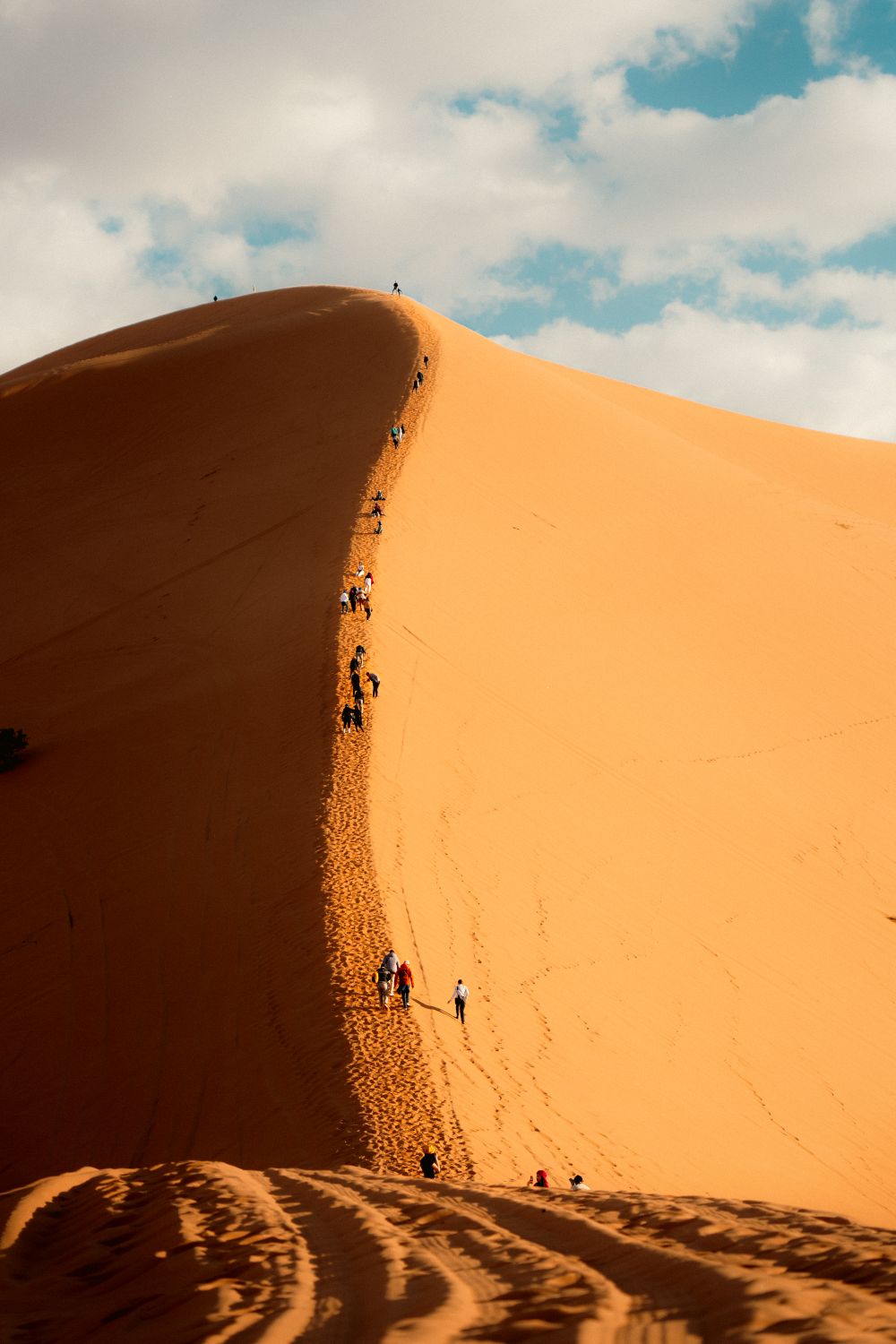 Photographer: Othmane Ettalbi Silhouettes of people ascending a towering sand dune against a bright blue sky in Namibia