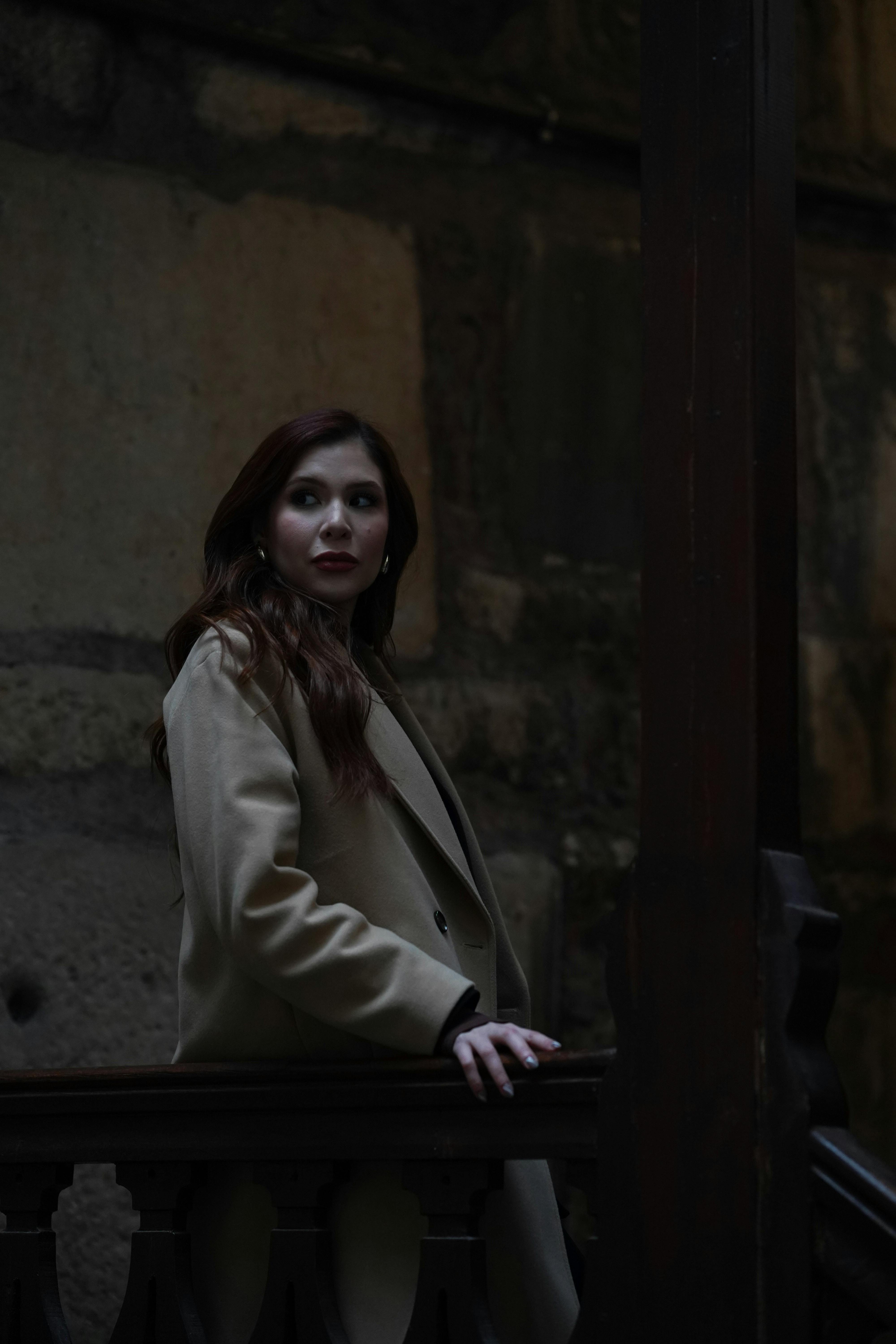 Stylish woman in a coat posing indoors with a dramatic moody ambiance.