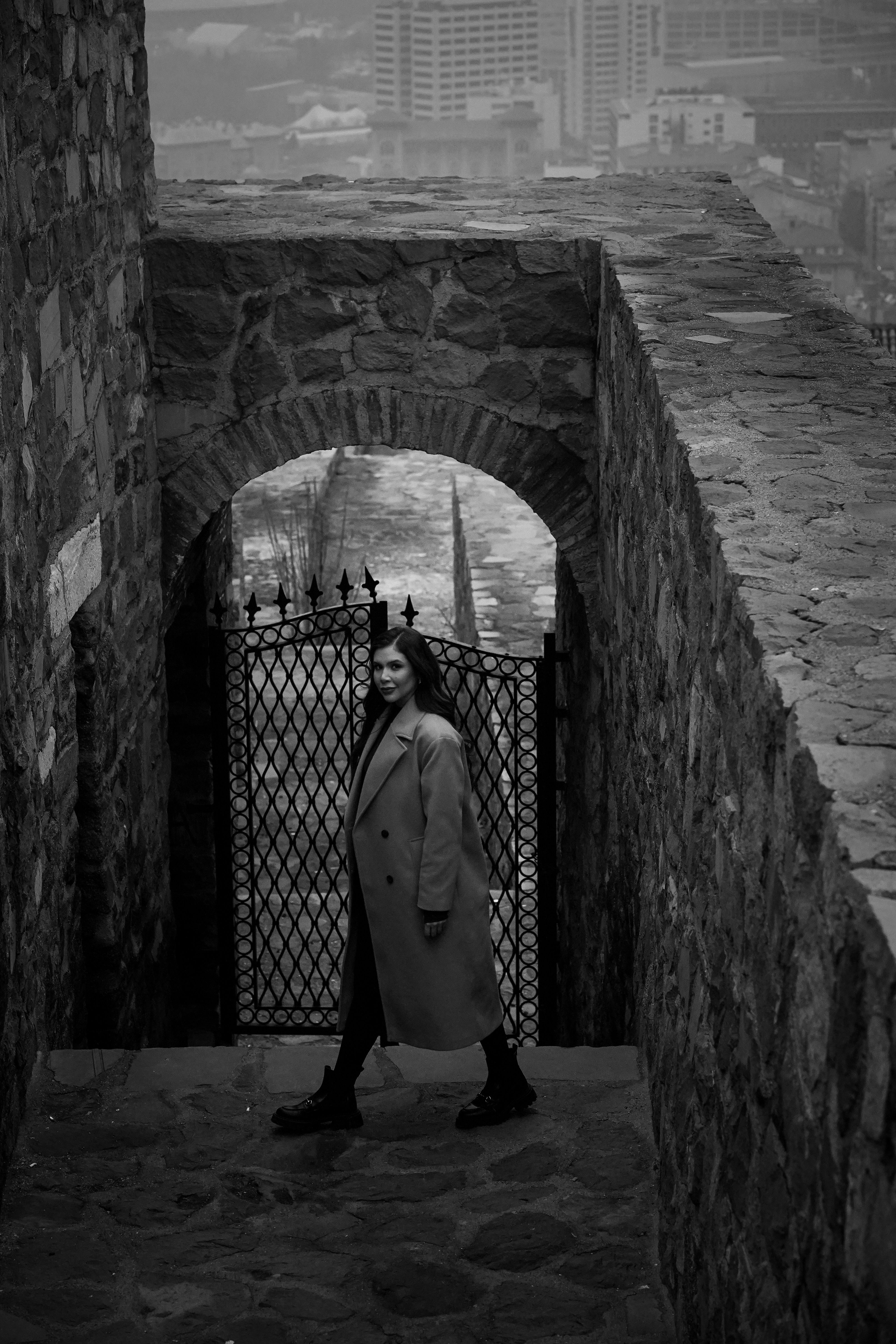 Woman in a Coat Walking Through Stone Archway · Free Stock Photo