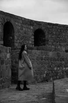 Black and white photo of a woman in a coat against an ancient stone wall.