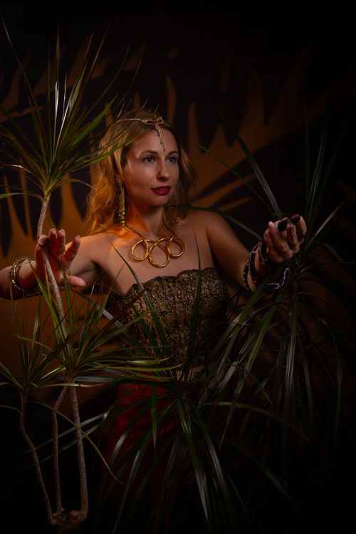 Free Woman in elaborate costume posing with tropical plants in moody lighting. Stock Photo
