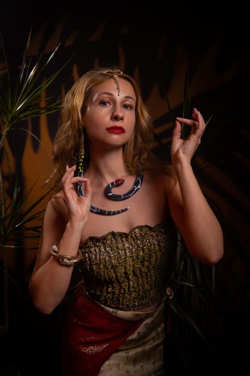 Free Stylish woman in ornate outfit posing amidst plants holding accessories. Stock Photo