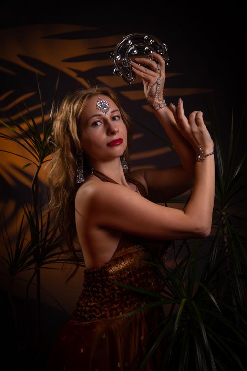 Free Elegant woman with jewelry dances holding a tambourine in a dramatic light. Stock Photo