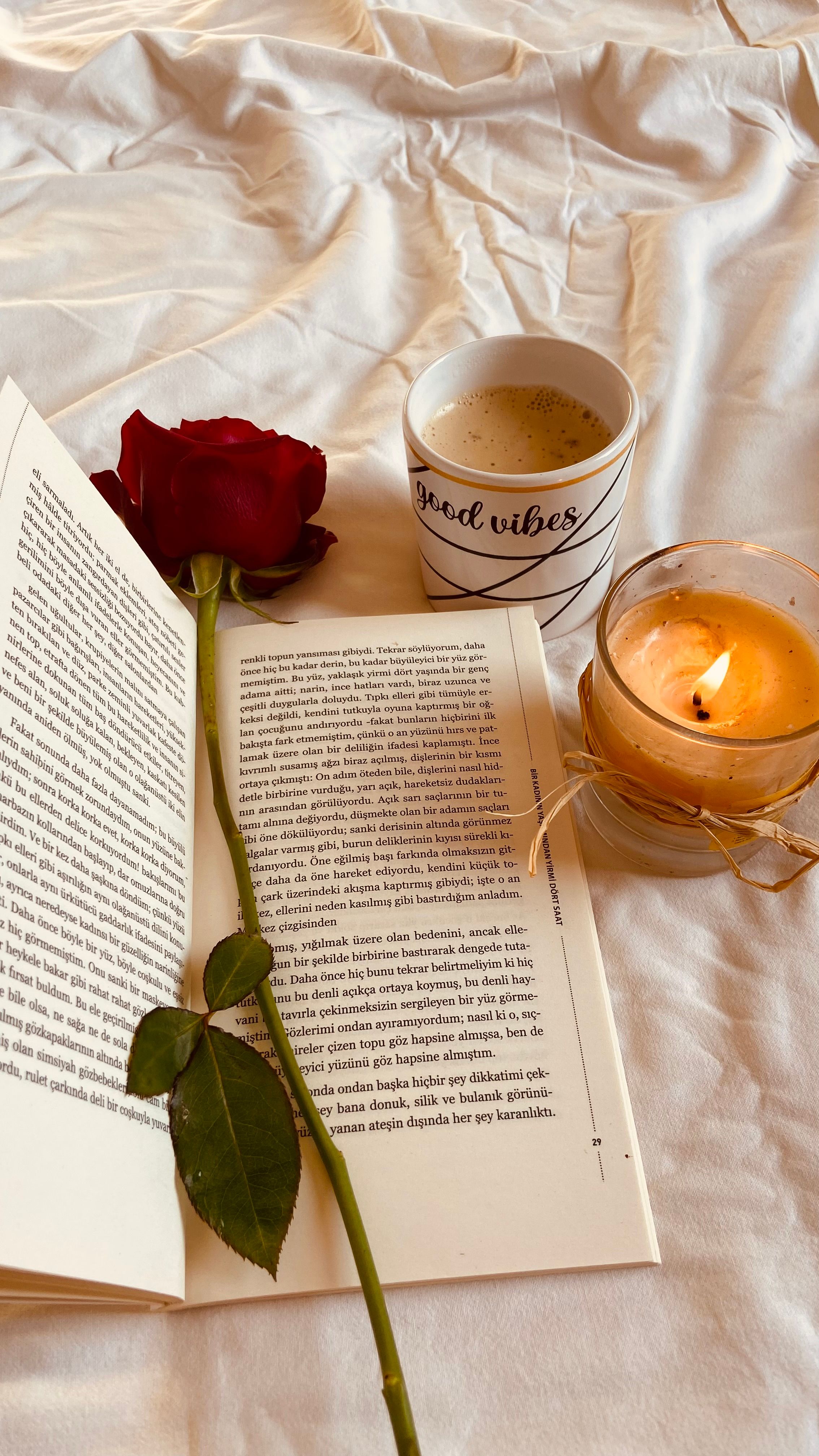 A comforting scene with a book, a red rose, candlelight, and a coffee cup labeled 'good vibes'.