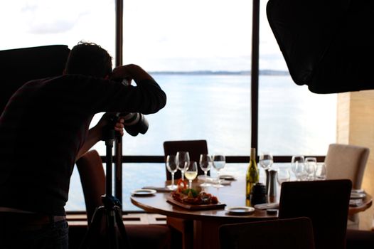 Photographer shoots a beautifully arranged restaurant table by the sea. Elegant setup with food and wine.