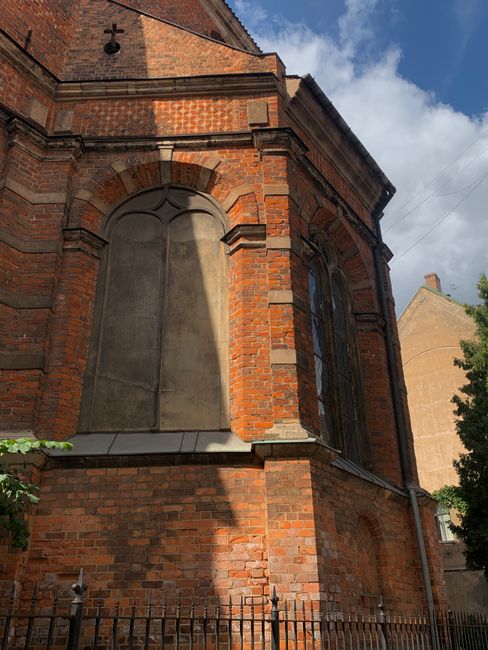 A detailed view of a historic red brick church with Gothic architectural elements, basking in sunlight.