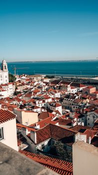 Aerial view of Lisbon's iconic red rooftops against a clear blue ocean backdrop.