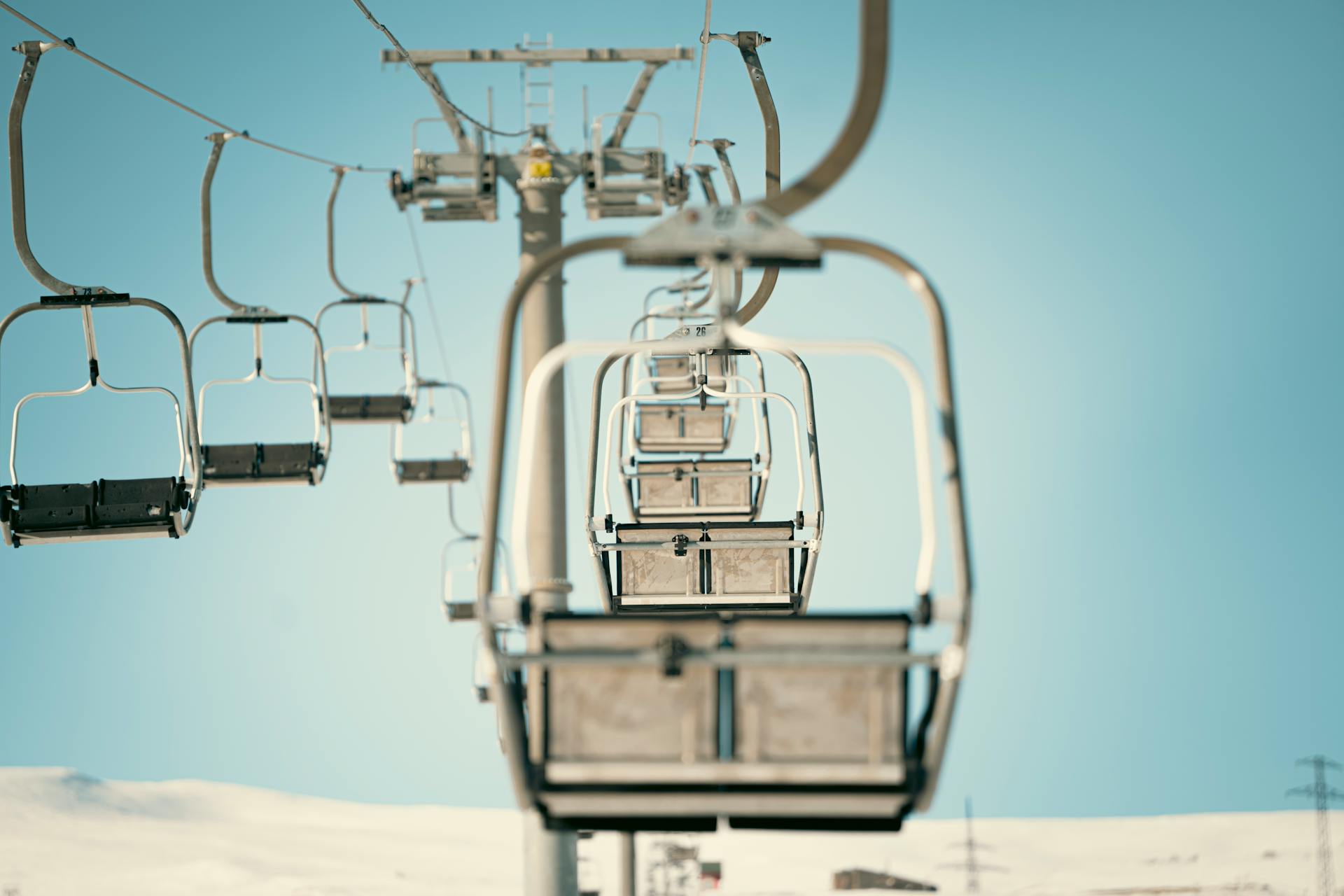 A row of empty ski lift chairs captured from below with a clear sky in the background, depicting winter sports facilities.