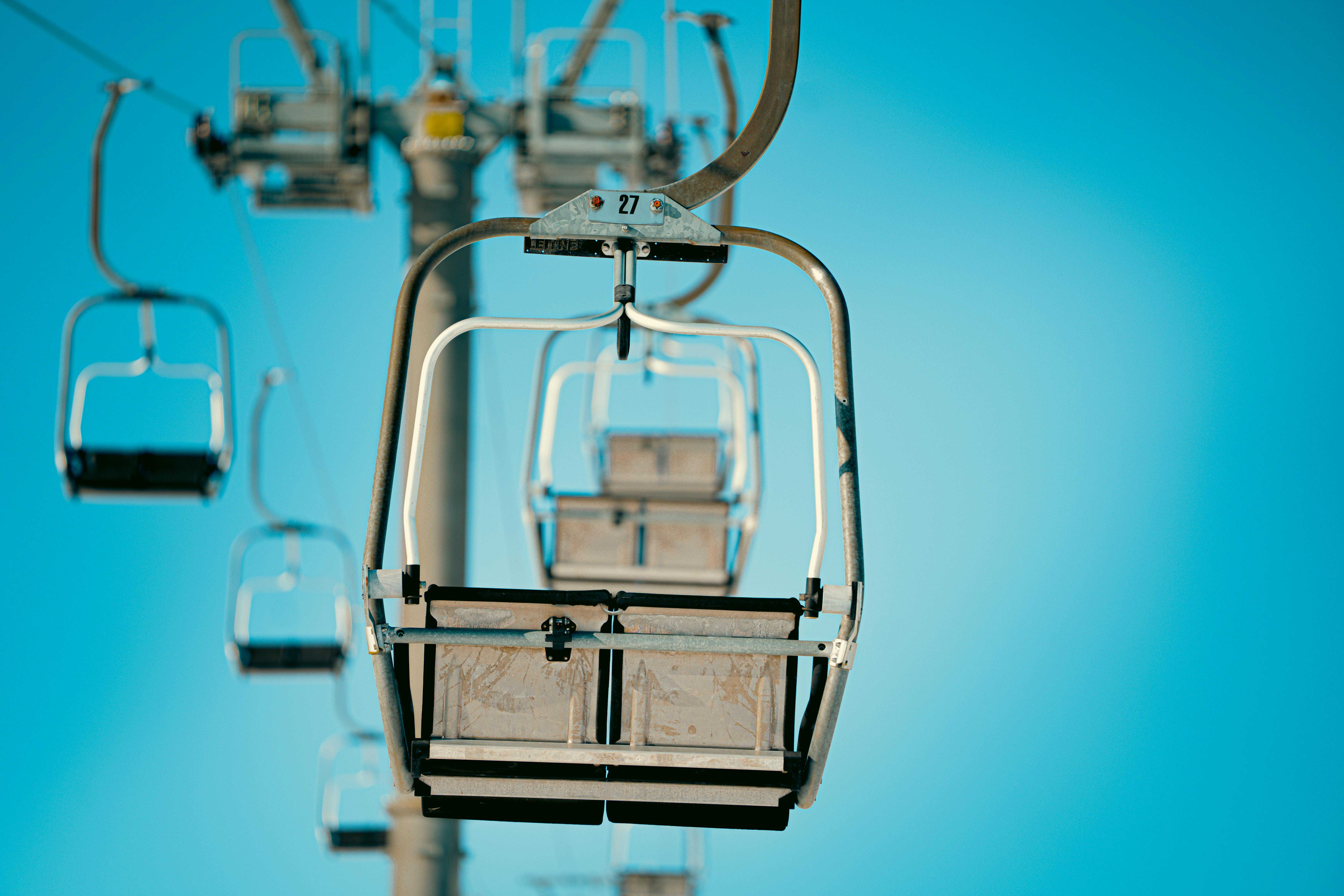 Close-up view of empty ski lift chairs in a line against a clear blue sky, conveying a sense of tranquility and anticipation.