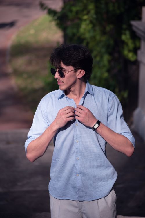 Free A young man with sunglasses adjusts his shirt outdoors on a sunny day. Stock Photo
