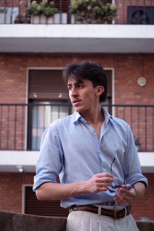 Free Young man in Buenos Aires stands stylishly in natural light, holding sunglasses. Stock Photo