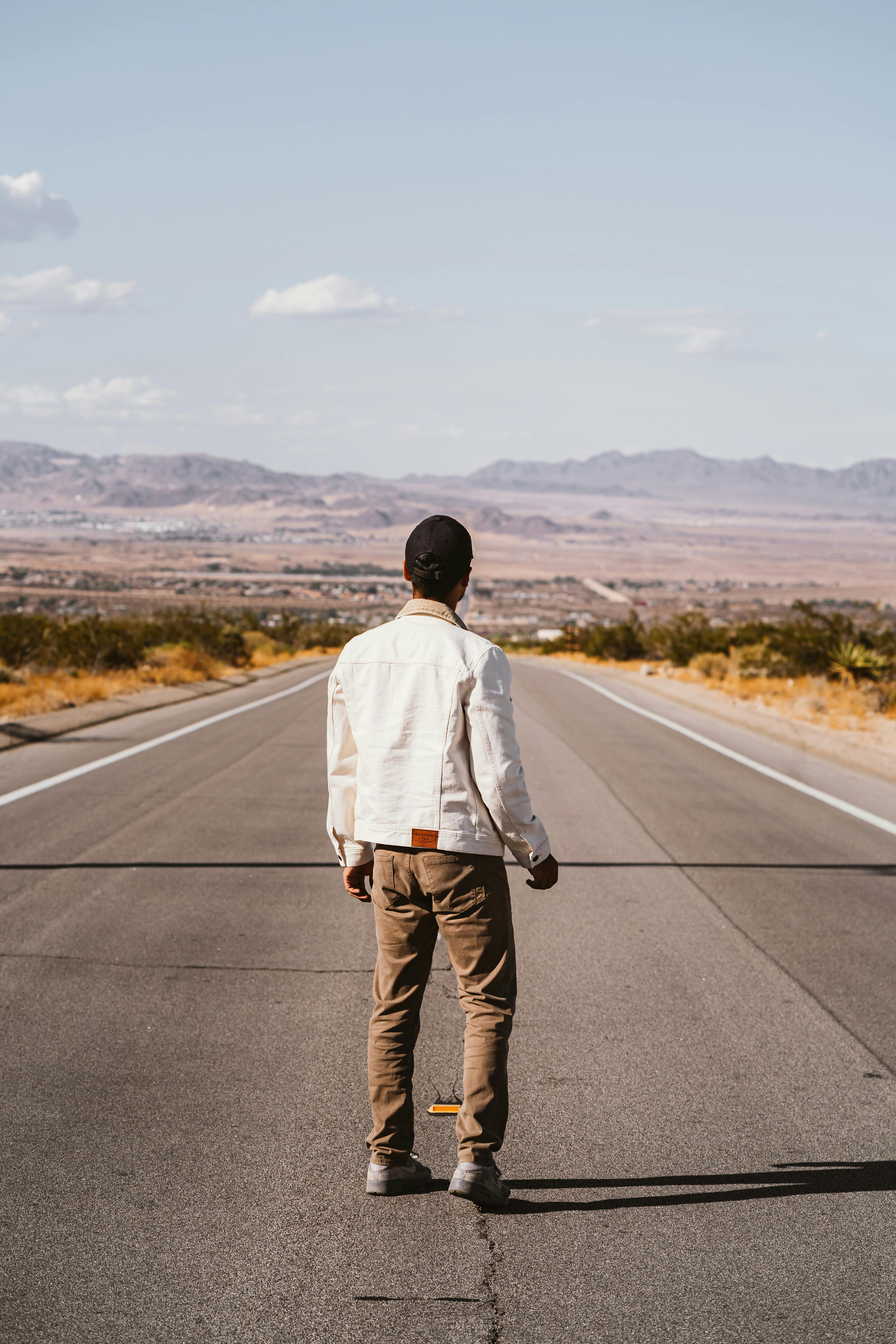 一名男子穿着白夹克，站在空旷的沙漠道路上，象征着孤独和冒险