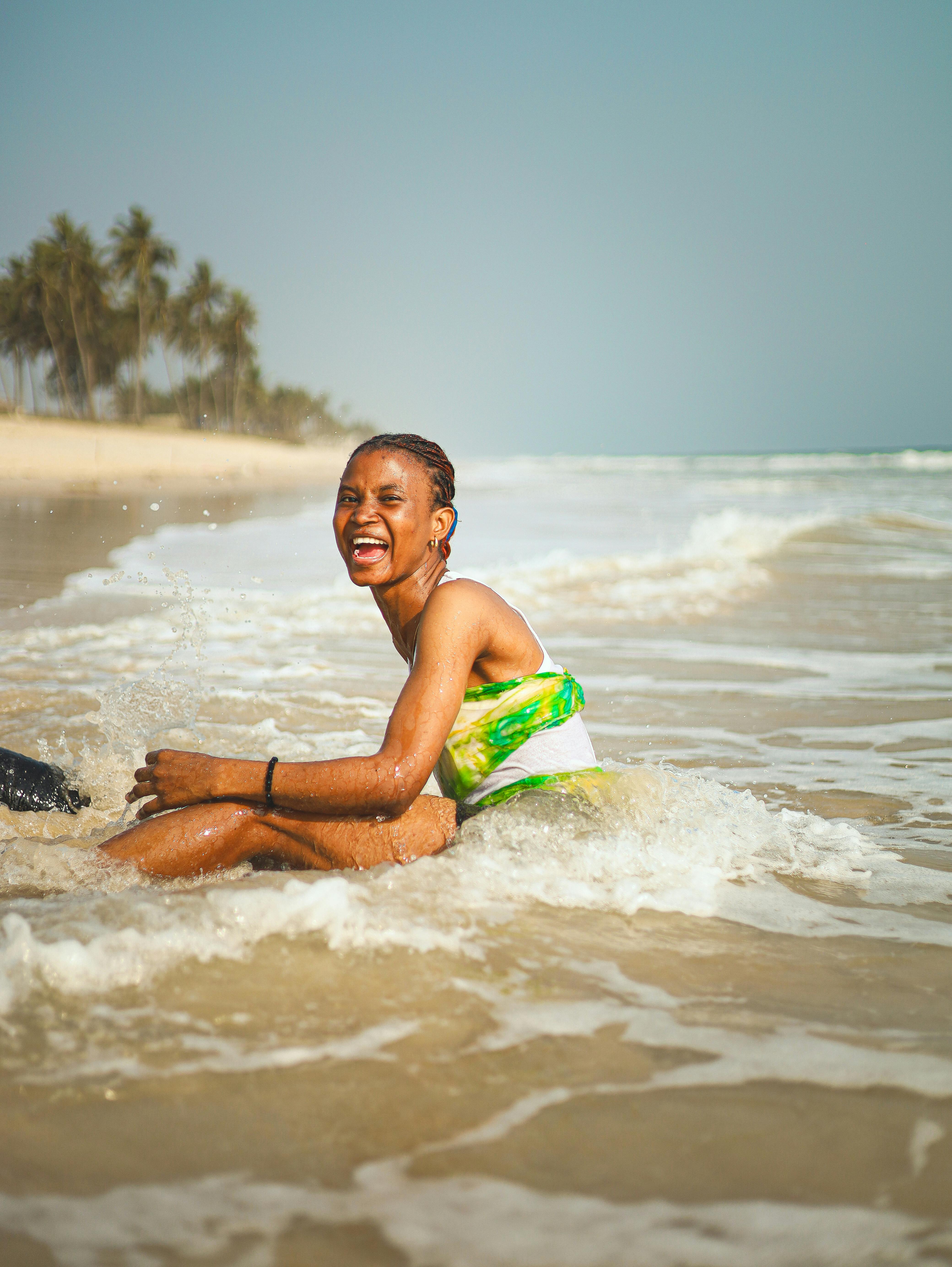 A woman laughing and playing in the ocean waves on a sunny beach day.