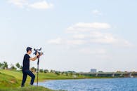 阳光明媚的日子里，一位男摄影师用三脚架在户外拍摄湖景