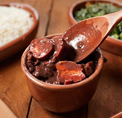 Gratis Un primo piano della tradizionale feijoada brasiliana servita in una pentola di terracotta con un cucchiaio di legno, che mette in risalto i gustosi ingredienti. Foto a disposizione