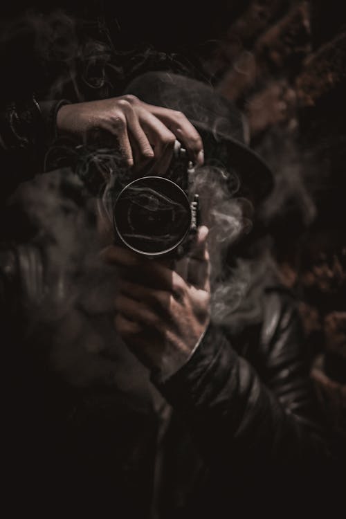 Man With Long Silver Gray Hair Wearing Black Jacket Holding A Camera To His Face