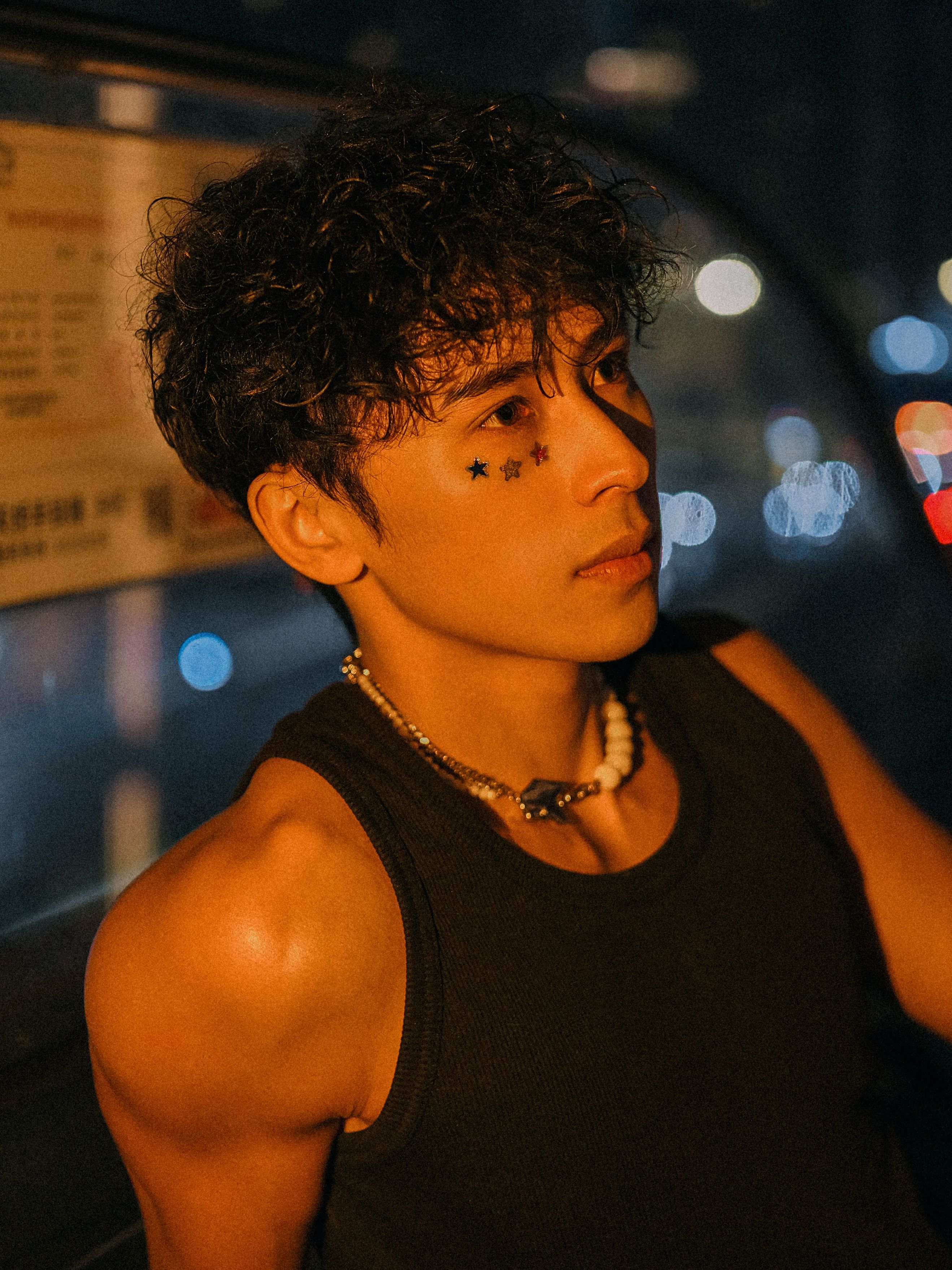 Fashionable young man with star face art posing in urban night setting with soft lighting.