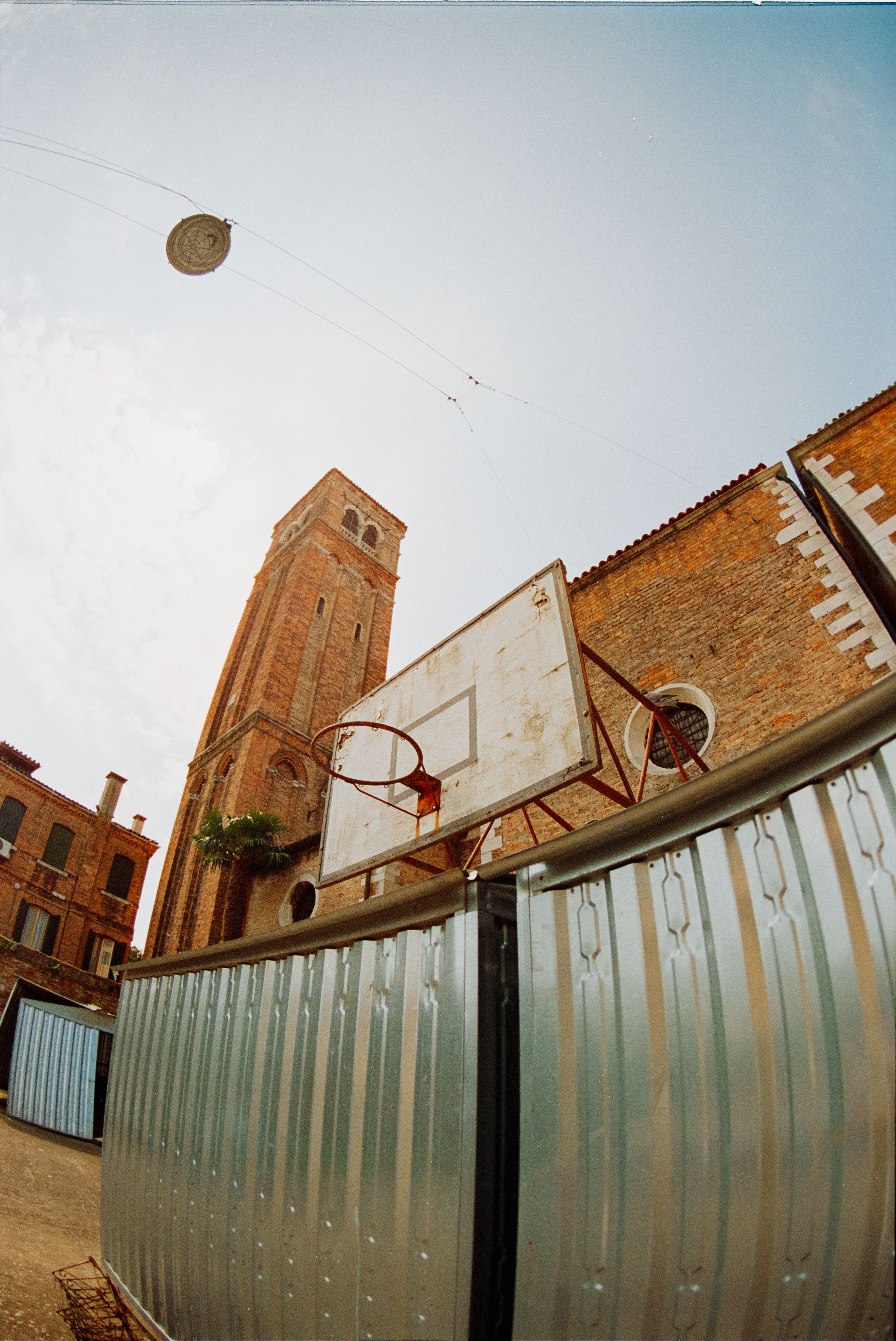 A basketball hoop stands against the backdrop of a historic tower in a vibrant, rustic setting.