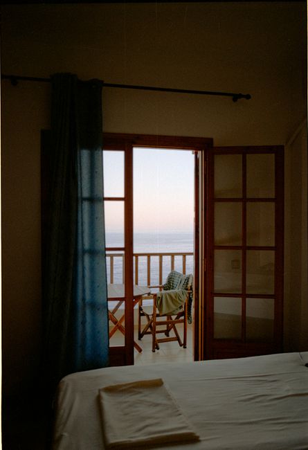Serene bedroom with open balcony doors overlooking the ocean at sunset for relaxation.