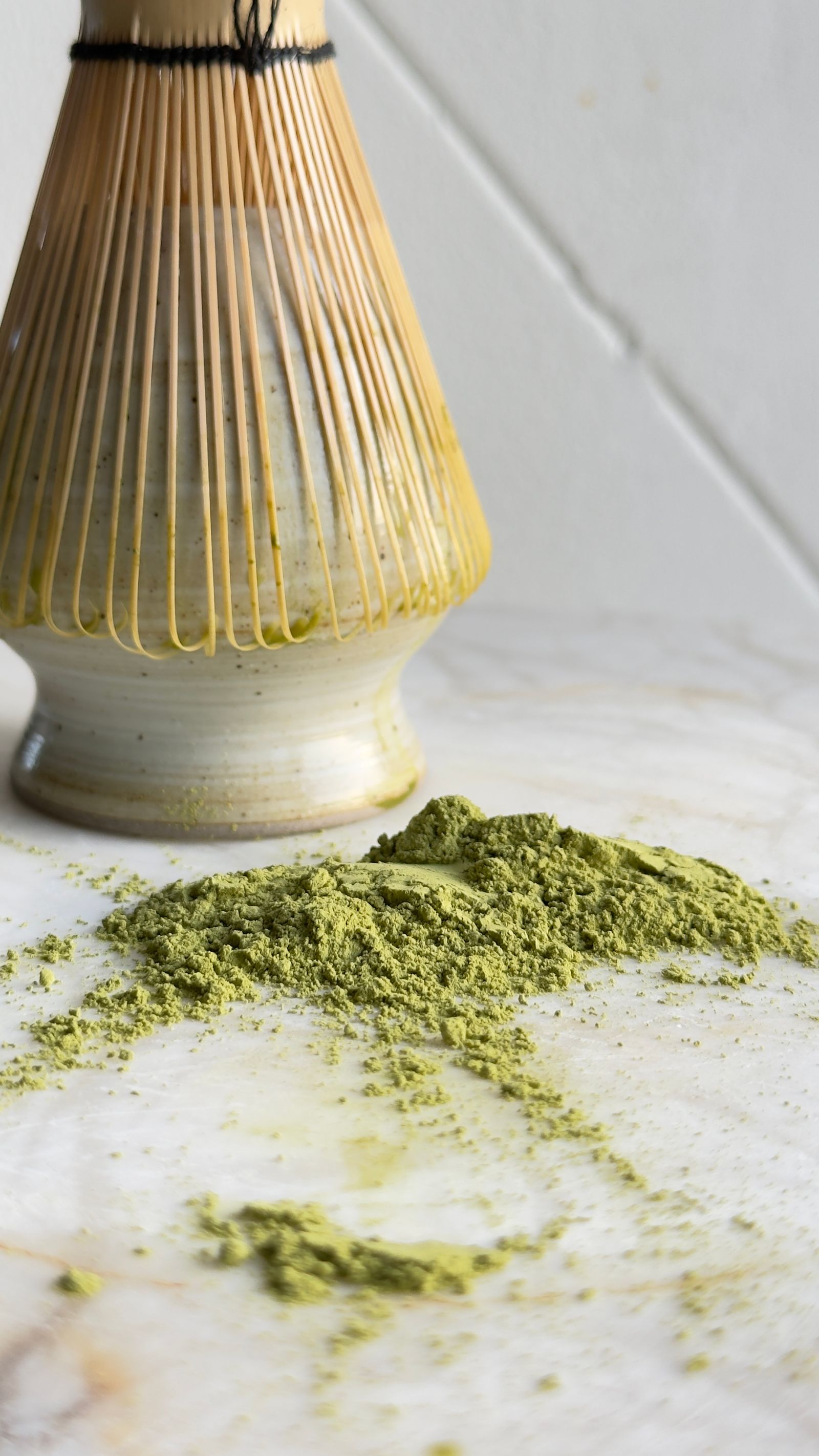 Fine matcha powder beside a bamboo whisk for making a smooth homemade latte