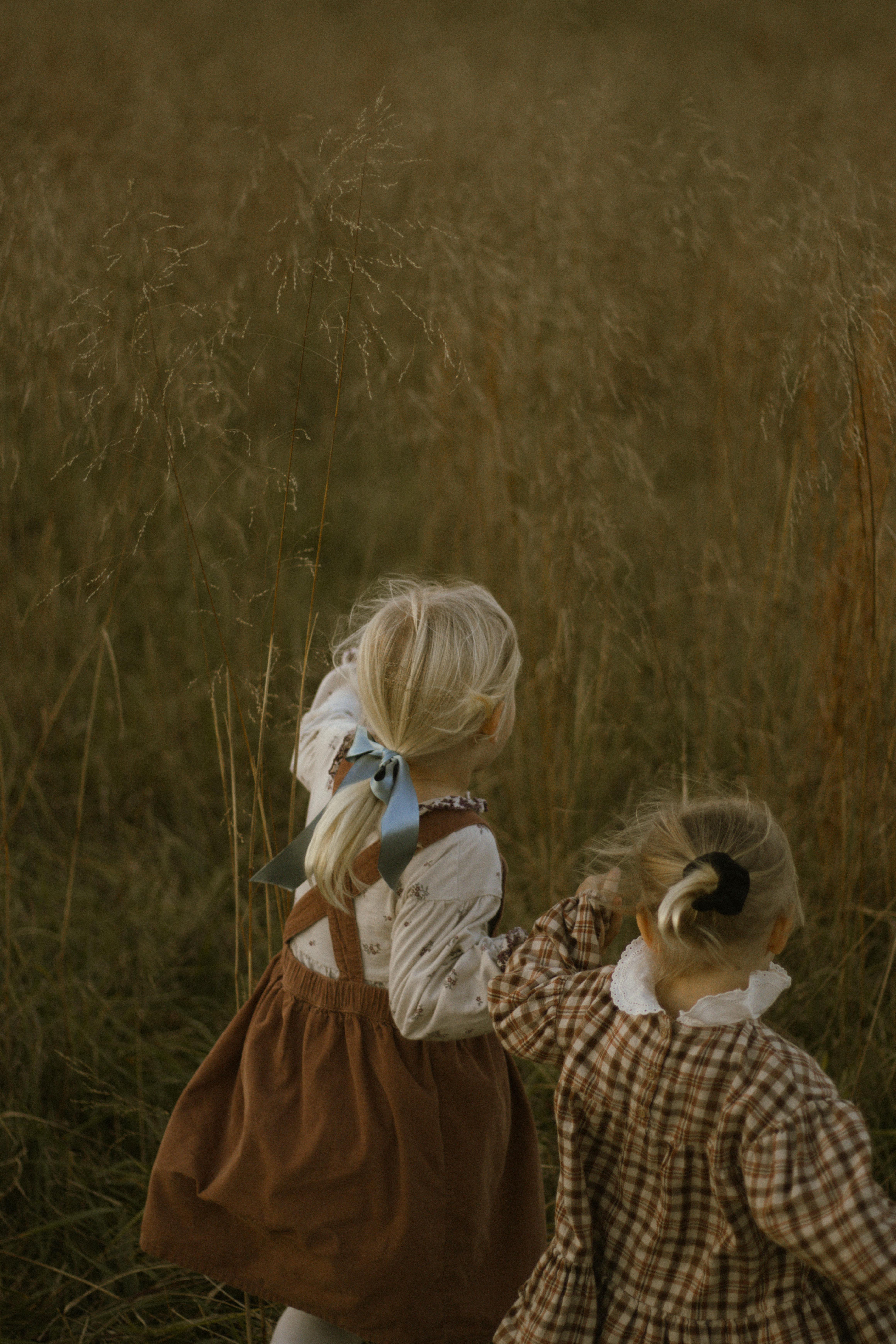Two young girls play joyfully in a grassy field during golden hour.