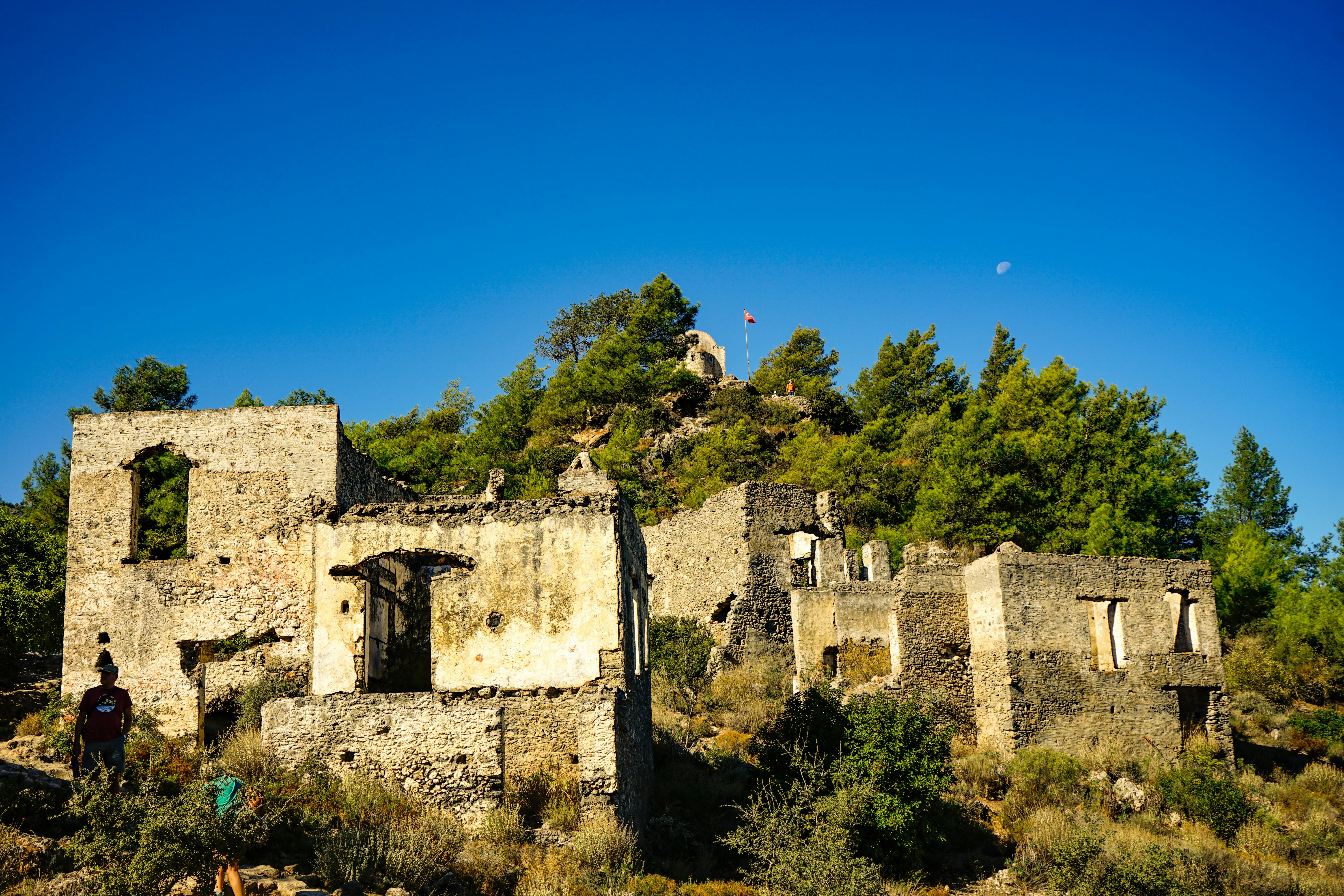 Explore the fascinating historical ruins of Kayaköy, Türkiye, surrounded by lush greenery and a bright, clear sky.